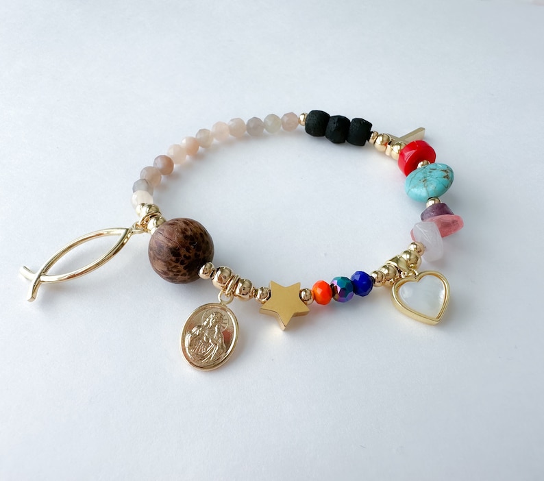 May include: A colorful beaded bracelet with a variety of charms, including a wooden bead, a star, a heart, and a religious medal. The bracelet is made with gold-toned beads and has a fish charm.