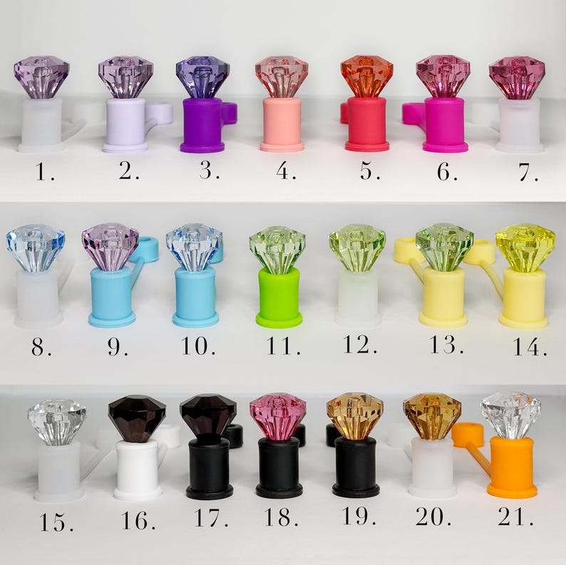 May include: A collection of twenty-one decorative bottle stoppers, each featuring a faceted gem-like top in various colors. The stoppers have a cylindrical base and a handle. Colors include clear, purple, pink, red, and yellow.