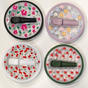 Pode incluir: Quatro recipientes redondos decorativos com tampa transparente e base colorida. Cada recipiente tem um design diferente: flores de hibisco rosa, flores pastel, cerejas vermelhas e cogumelos vermelhos. Cada recipiente cont&eacute;m um aplicador colorido correspondente.
