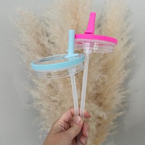 Pode incluir: Duas tampas de copo de pl&aacute;stico transparente com canudos. Uma tampa &eacute; azul claro, a outra rosa choque. As tampas t&ecirc;m uma base de pl&aacute;stico transparente e um topo colorido correspondente com um orif&iacute;cio para canudo. Os canudos s&atilde;o de pl&aacute;stico transparente.