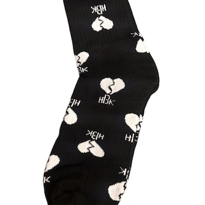 May include: Black crew sock with a repeating pattern of white broken hearts. The letters "HBK" are printed below each heart. The sock is made of a soft, comfortable material.