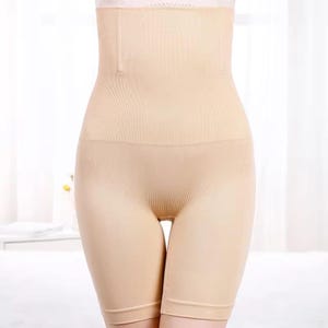 Könnte beinhalten: Beige Shapewear mit hohem Bund. Das Kleidungsstück ist nahtlos und reicht von der Mitte des Oberschenkels bis zur Mitte des Bauches. Das Material ist gerippt und figurbetont, in einer neutralen Farbe.