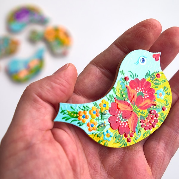 以下が含まれることがあります： 手描きの木製鳥型オーナメント。鳥は水色、黄色、赤で塗装され、花のディテールが施されています。鳥の長さは約7.6cmです。