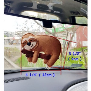 Puede incluir: Un perezoso marrón colgado de una rama, con los ojos cerrados, como si estuviera durmiendo. El perezoso mide 12 cm de ancho y 9 cm de alto.