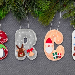 May include: Felt Christmas ornaments shaped like the letters S, R, C, and L. Each letter has a different festive character: a gnome, a reindeer, Santa Claus, and a gingerbread man.