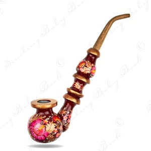 Puede incluir: Una pipa de tabaco pintada a mano con un acabado rojo oscuro y diseños florales en rosa, naranja y amarillo. La pipa tiene una boquilla de madera y detalles dorados. El cuenco es redondo y el tallo es curvo.