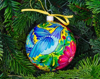 May include: A yellow Christmas ornament with a blue bird and floral design. The ornament is hand-painted with vibrant colors and intricate details.
