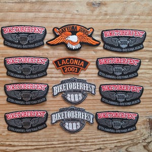 May include: A collection of embroidered patches with motorcycle rally themes. The patches feature text like "BIKETOBERFEST" and "DAYTONA BEACH" with years such as 2005, 2009, and 2013. Designs include eagles and wings, in red, black, and orange.