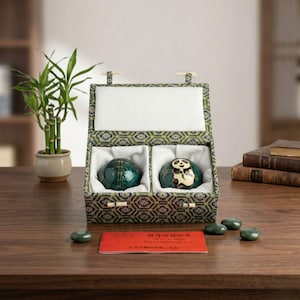 May include: A set of two green exercise balls in a patterned box. One ball has a panda design, the other has a geometric pattern. The box is open, revealing the balls nestled in white fabric. A red card and several small green stones are also visible.