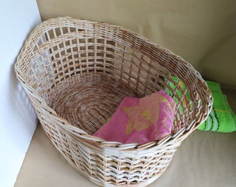 May include: A white wicker oval laundry basket with a pink towel with yellow floral design inside and a green towel on the side.