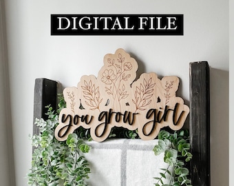 May include: A wooden sign with the text "you grow girl" in black lettering. The sign is decorated with a floral design and is displayed against a white and grey background.