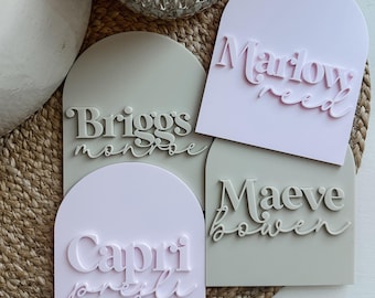 May include: Four arched name tags with different names and last names. The tags are in pink and gray with white lettering. The names are "Briggs Monroe", "Marlow Reed", "Maeve Bowen", and "Capri Presley".