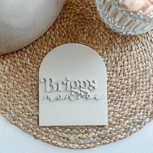 May include: A white arch-shaped sign with the name "Briggs Monroe" written in a stylized font.
