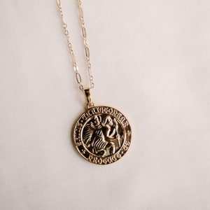 May include: Gold chain necklace with a round pendant featuring a detailed image of Saint Christopher. The pendant has the words "Sanctus Christopher" and "Protector" inscribed around the edge.