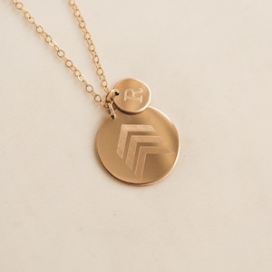May include: Gold necklace with two round pendants. The larger pendant has an engraved chevron design. The smaller pendant has the letter "R" engraved on it.