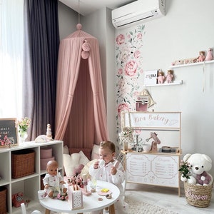 May include: A pink and white play kitchen with a sign that says "Kira Bakery." The kitchen has a cash register, a coffee maker, and a display shelf. There are also some toy pastries and a teddy bear in a basket.