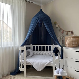 May include: A white crib with a blue canopy and a white braided bumper. A white bunny-shaped stool sits next to the crib. A white rug with fringe is on the floor.