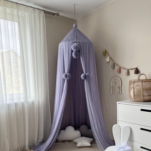 May include: A light purple canopy with pom poms hangs over a round rug with tassels. A white bunny chair with pom poms sits in the corner of the room.