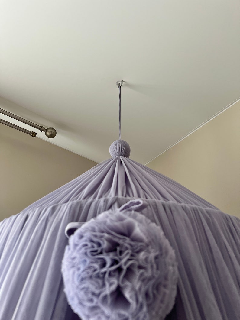May include: A lavender-colored canopy with a large, ruffled pom-pom hanging from the center.