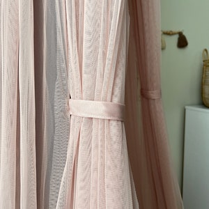 May include: A pink sheer canopy with a white ribbon tie. The canopy is made of a delicate, lightweight fabric and is perfect for creating a cozy and romantic atmosphere.