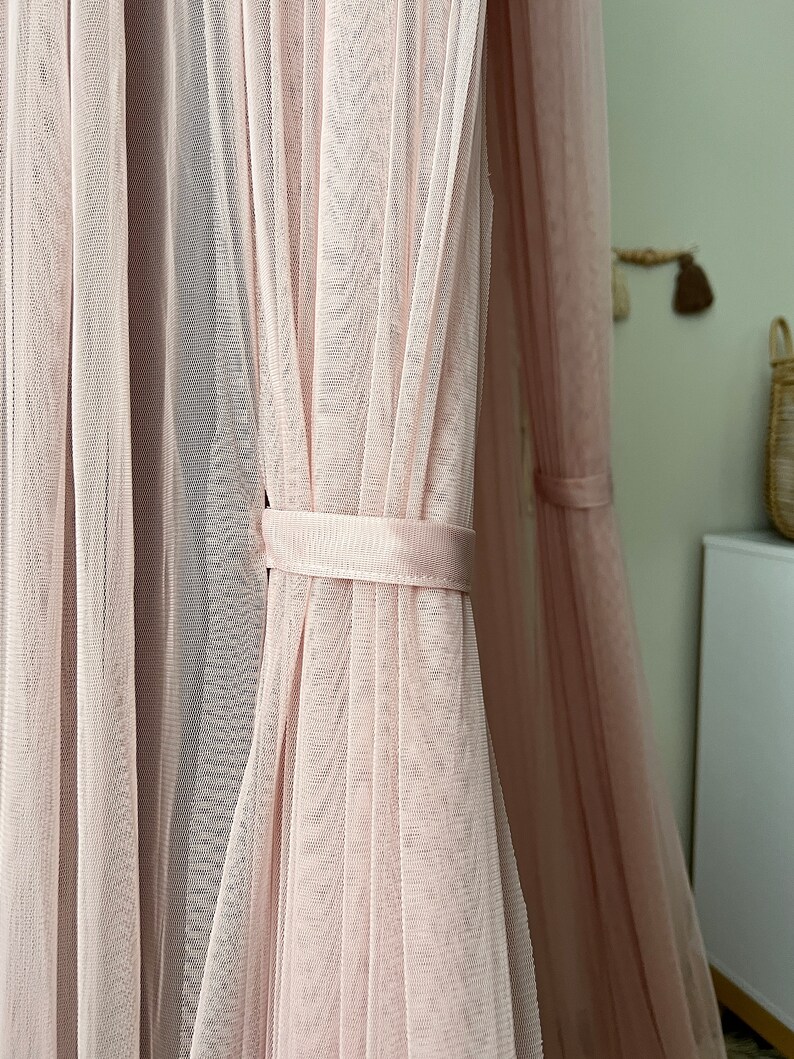 May include: A pink sheer canopy with a white ribbon tie. The canopy is made of a delicate, lightweight fabric and is perfect for creating a cozy and romantic atmosphere.