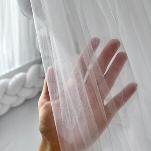 Puede incluir: Una mano se extiende a trav&eacute;s de una cortina blanca transparente, la tela es delicada y transl&uacute;cida.