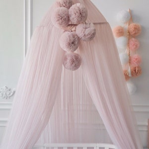 May include: A pink tulle canopy with a white crib underneath. The canopy has a cluster of pink pom-poms hanging from it. The text #7. Antik is visible in the bottom left corner of the image.