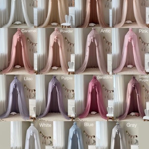 May include: A collection of 15 different colored tulle canopy beds with pom poms on top. The canopies are arranged in three rows of five. The colors are: Milk, Nude, Cocoa, Peach, Caramel, Powder, Antic, Pink, Lilac, Purple, Geraldine, Smoky Purple, White, Blue, and Gray.