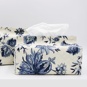 May include: Two tissue box covers with a floral pattern. The larger cover is white with blue floral designs and the smaller cover is white with blue floral designs and a bird.