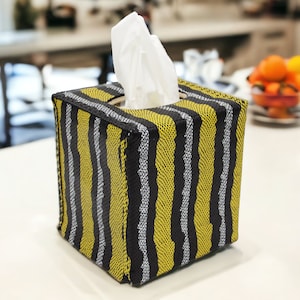 Könnte beinhalten: Eine gelbe und schwarze gestreifte Tissuebox mit einem weißen Gewebespender.