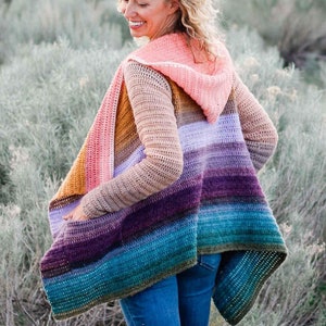 May include: A multi-colored crochet cardigan with a hood. The cardigan is made with a variety of shades of blue, purple, pink, and brown yarn. The cardigan is open in the front and has long sleeves.