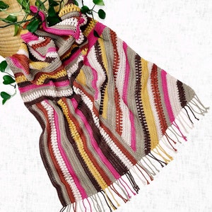 Könnte beinhalten: Eine gestreifte gehäkelte Wolldecke mit Fransen in den Farben Braun, Rosa, Beige und Gelb.