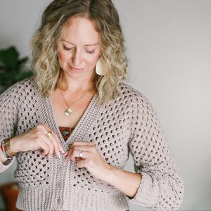 A woman buttoning her hexagon cardigan paired with a brown jumper.
