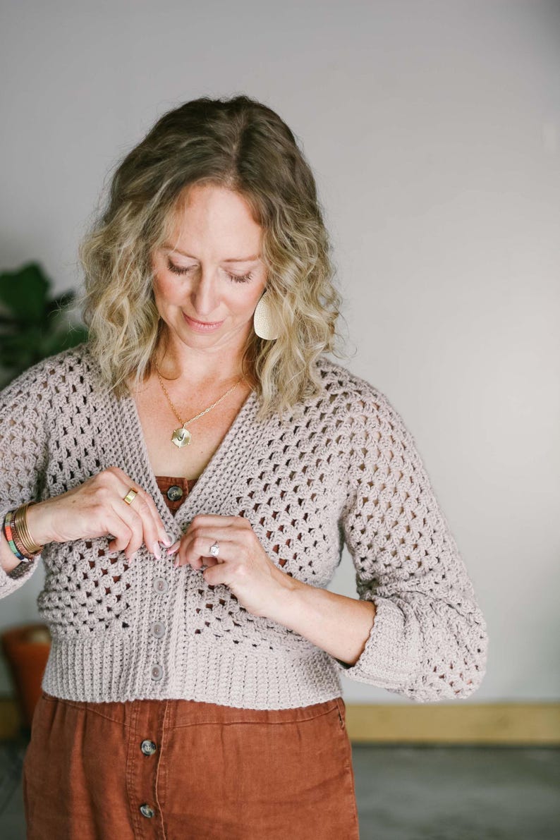 A woman buttoning her hexagon cardigan paired with a brown jumper.