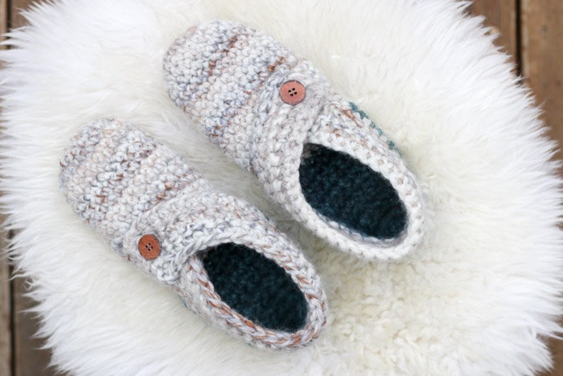 A pair of white house shoes with a button detail placed on a white fur rug.