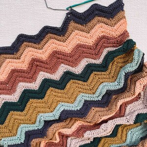 May include: A multi-colored crocheted blanket with a zig-zag pattern in shades of brown, pink, green, blue, and gray.