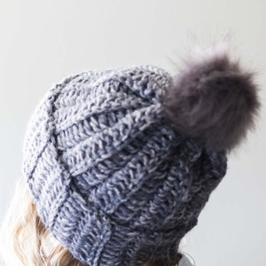 A blonde woman wearing a gray easy adult beanie with a pom pom.