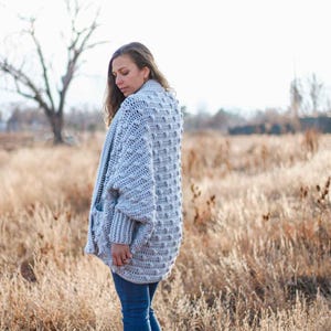 An oversized crochet sweater worn by a woman standing on a field.