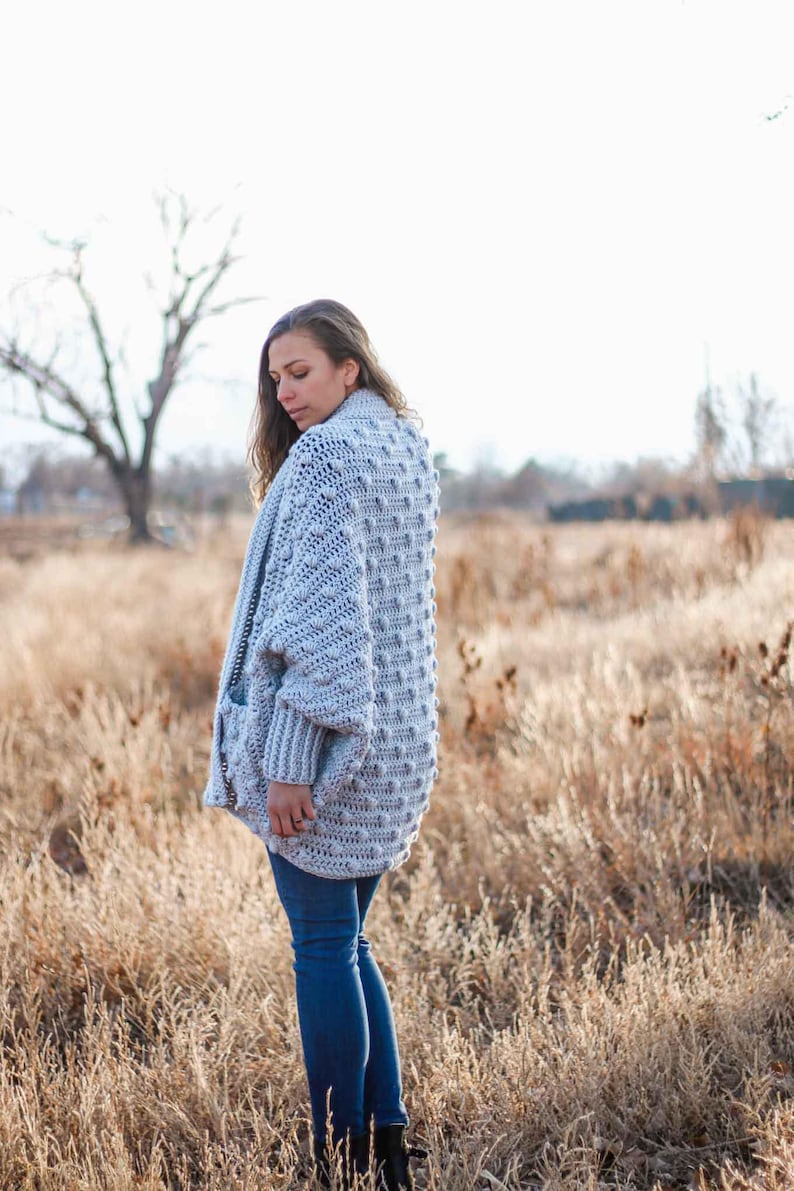 An oversized crochet sweater worn by a woman standing on a field.