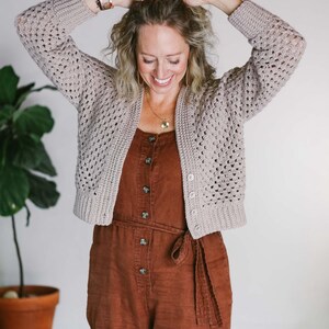 A cropped cardi worn by a woman with a brown jumper with her hands on her hair.