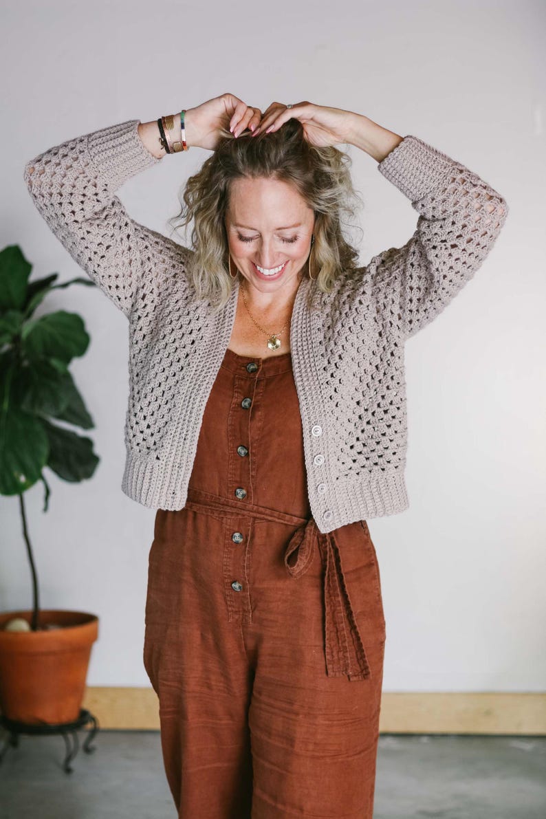 A cropped cardi worn by a woman with a brown jumper with her hands on her hair.