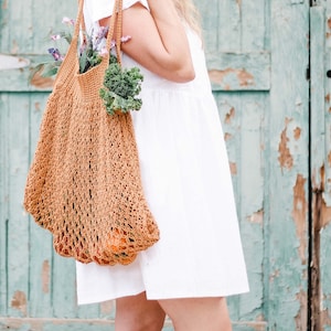 A blonde woman is carrying an easy-tote bag full of vegetables, fruits, and flowers.