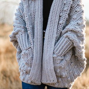 A chunky, winter rectangle cardigan worn by a woman standing on a field.