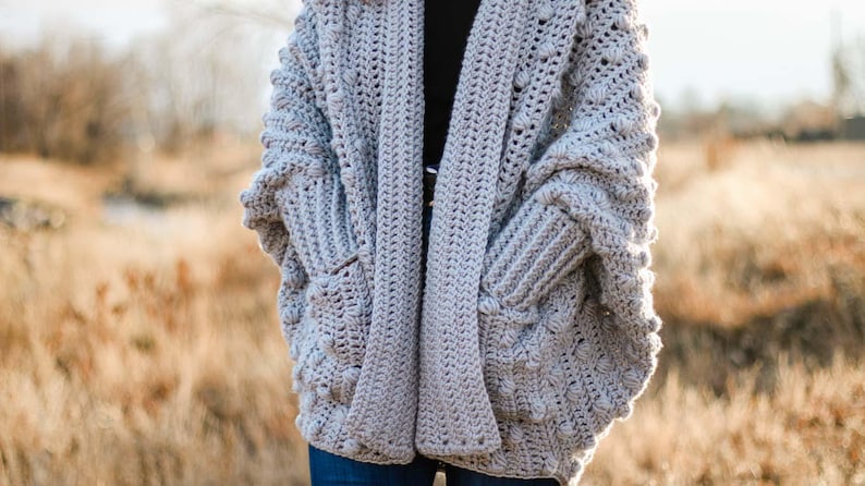 A chunky, winter rectangle cardigan worn by a woman standing on a field.