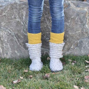 A woman wearing a pair of comfy gray sweater boots, yellow socks, and denim jeans.