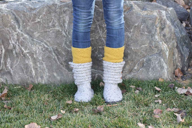 A woman wearing a pair of comfy gray sweater boots, yellow socks, and denim jeans.