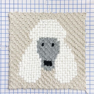 May include: A crocheted wall hanging featuring a white poodle with a grey face and black nose. The poodle is surrounded by a beige background.