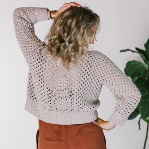 A hexagon cardigan worn by a woman paired with a brown jumper with her hand on her hair and the other on her hip with her back to the camera.