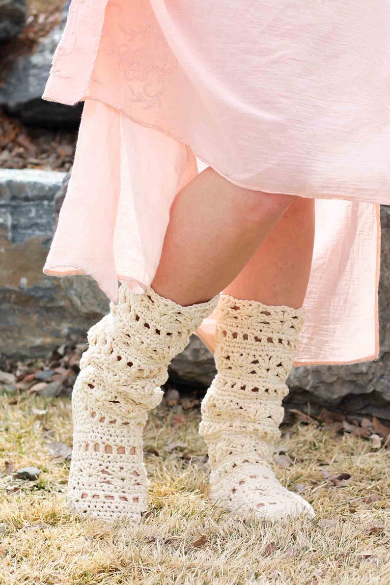A woman standing on a grass field wearing a pink dress and a pair of lacy crochet shoes.