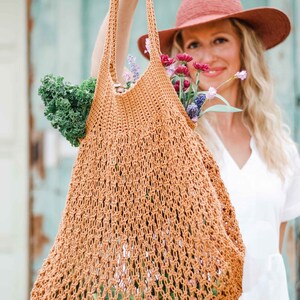 A blonde woman is holding a farmer's market bag full of vegetables, fruits, and a bunch of flowers.